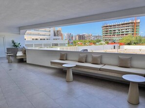 Ein moderner Außenbereich mit einer Couch und zwei runden Tischen, mit Blick auf eine Stadtlandschaft inklusive Gebäude und Bauarbeiten.