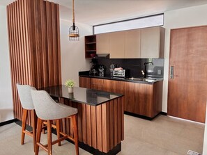 Eine moderne Küche mit Holzschränken, einer schwarzen Arbeitsplatte und einer kleinen Kochinsel mit zwei Stühlen.