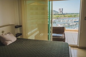 Ein Schlafzimmer mit Bett, Kissen, Stuhl und Blick auf eine Marina durch eine Glastür.