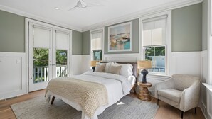 Un dormitorio con una cama, una silla, un cuadro y una ventana.
