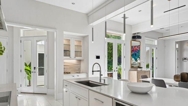 Una cocina moderna con armarios blancos, una isla grande con un lavamanos y una zona de comedor con una mesa y sillas.