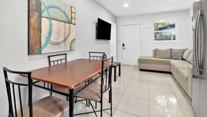 A modern living room with a dining table, chairs, a sofa, a flat-screen TV, and a large abstract painting on the wall. - Private 1BR Near Miami Airport with Free Parking (Hialeah)