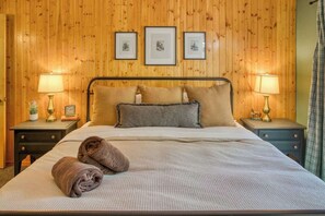 Ein Zimmer mit Holzwänden, einem Bett, zwei Nachttischen und gerahmten Bildern an der Wand.