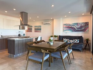 Une cuisine moderne avec un îlot central, un coin repas avec une table et des chaises en bois, un canapé agrémenté de coussins à motifs et un grand tableau abstrait accroché au mur.