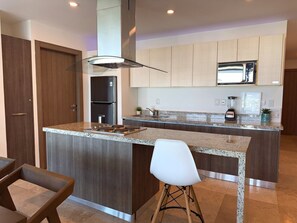 Una cocina moderna con una isla central, electrodomésticos integrados y una zona de comedor con una silla.