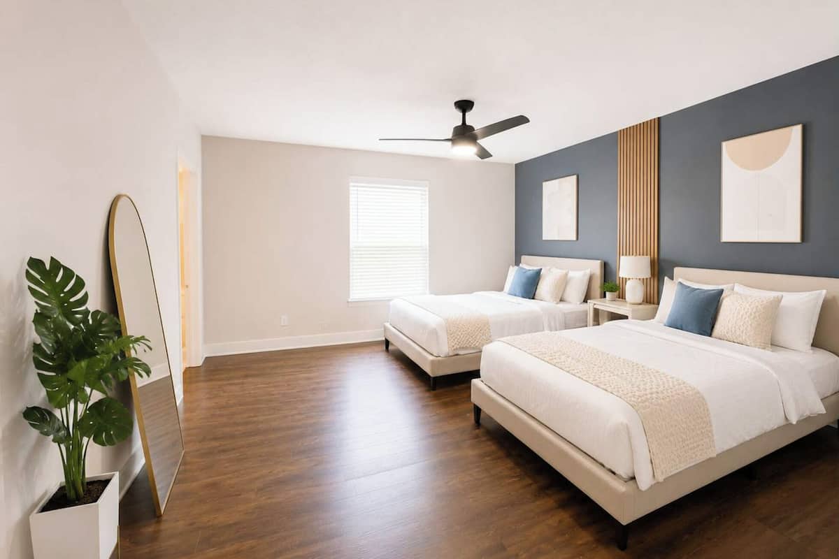 A bedroom with two beds, a ceiling fan, a large mirror, and a potted plant.