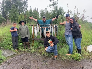 A group of people standing outdoors with a wooden rack holding several fish. - Private Kenai River fishing, no combat fishing here!!!!! Comfy cabins too! (Soldotna)