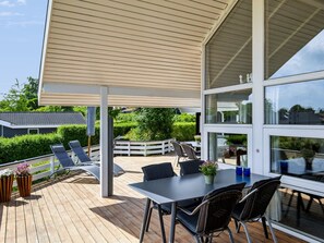 Een overdekt terras buiten, met een tafel en stoelen, een witte schutting en potplanten.