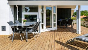 Eine überdachte Terrasse im Freien mit Tisch, Stühlen, einem Grill und einem Holzboden.