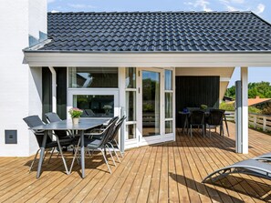 Un patio techado al aire libre con una mesa, sillas, una parrilla y una terraza de madera.