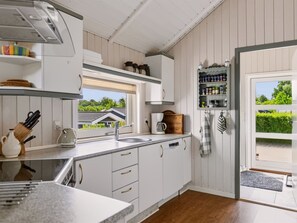 Cocina con armarios blancos, un lavamanos, una ventana y una puerta que da al exterior.