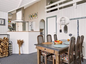 Een eetgedeelte met een houten tafel, stoelen, een fruitmand en een hanglamp.