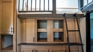 A loft-style bedroom with a bunk bed, wooden cabinetry, and a ladder.