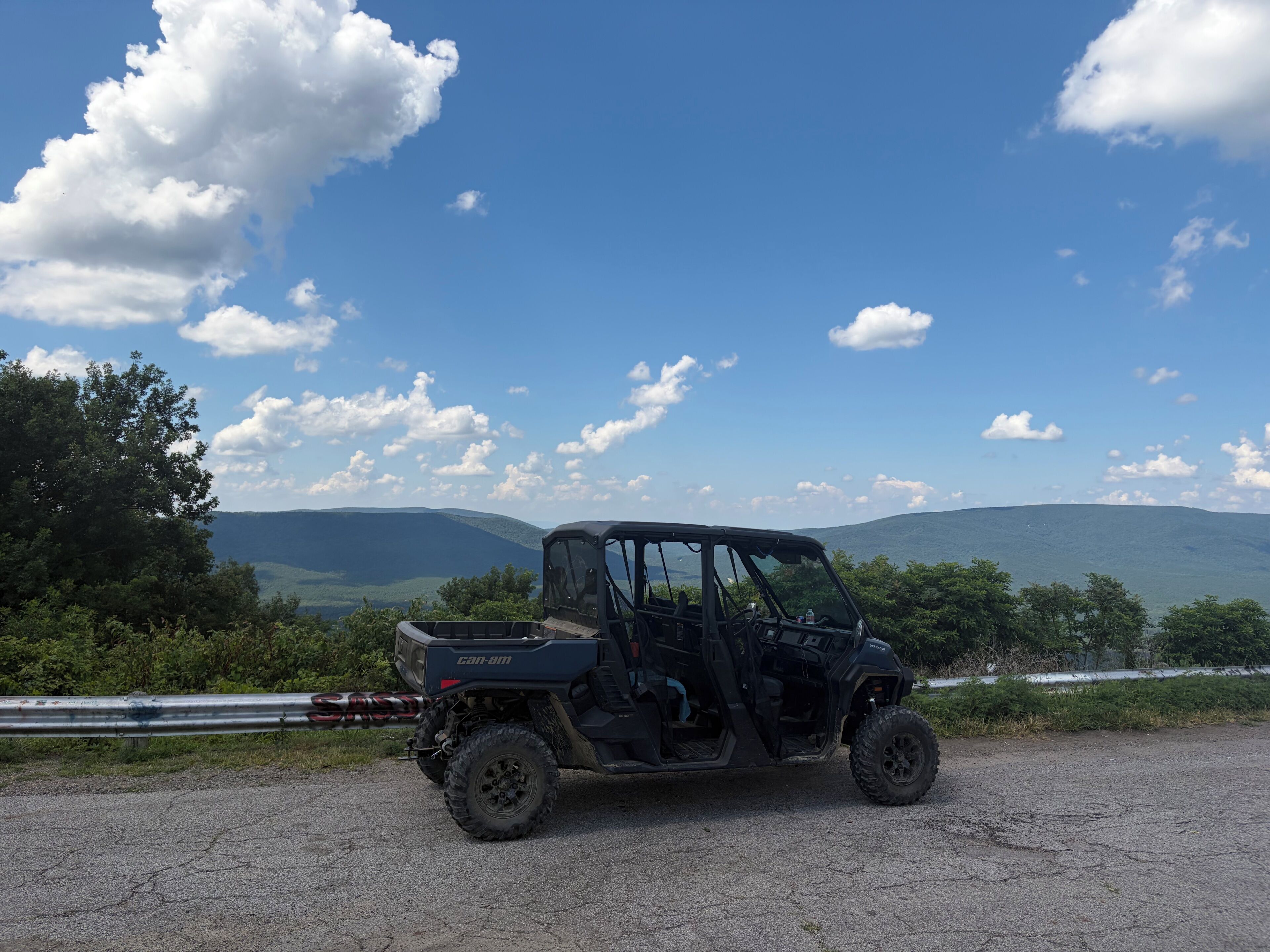 Un véhicule tout-terrain noir est garé sur un chemin de gravier, offrant une vue panoramique sur les montagnes et les arbres en arrière-plan.