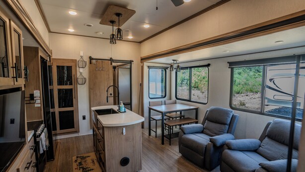 A compact RV interior with a kitchenette, seating area, and large windows.