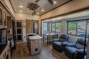 A compact RV interior with a kitchenette, seating area, and large windows.