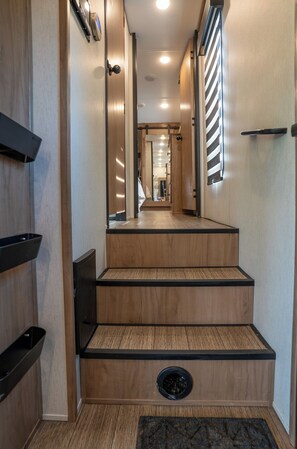 A wooden staircase with a black edge, a handrail, and a small vent at the bottom.