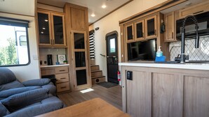 A compact RV kitchen with wooden cabinets, a built-in stove, and a seating area with gray cushions.