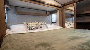 A bedroom with a bed, pillows, a headboard, a window, and a mirror.