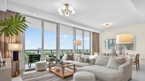 Ein geräumiges Wohnzimmer mit einer großen Eckcouch, einem Couchtisch und Blick auf die Stadt durch raumhohe Fenster.