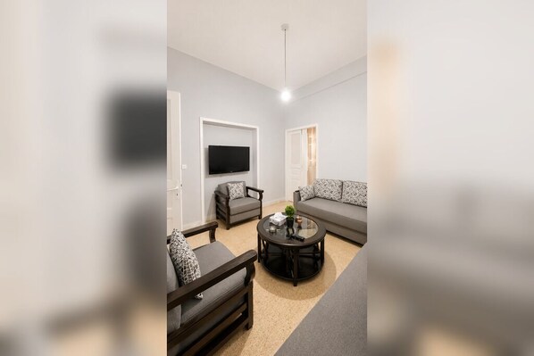 A modern living room with a sofa, two armchairs, a coffee table, and a flat-screen TV mounted on the wall.