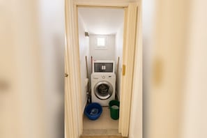 A laundry room with a washing machine, two buckets, and a window.