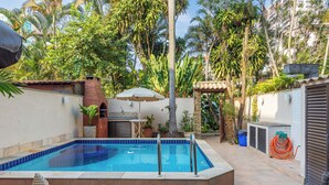 Ein Schwimmbecken mit gefliestem Deck, umgeben von einem Garten mit Palmen und einem Mauerwerk.