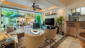 Ein modernes Wohnzimmer mit Fernseher, Sofa, Sesseln und einem Essbereich mit Tisch und Stühlen.