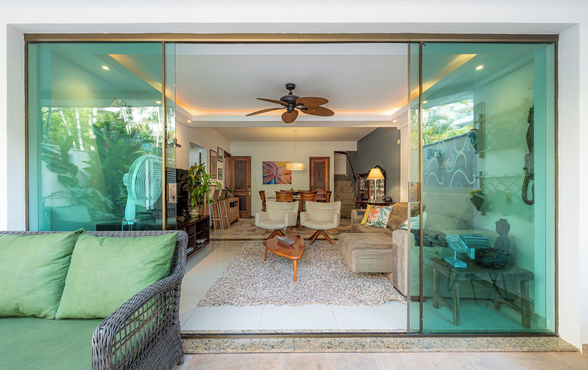 Un salon moderne doté d’une porte vitrée donnant sur une salle à manger, d’un ventilateur de plafond et offrant une vue sur la verdure environnante.