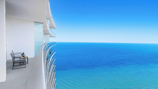 Un balcone con vista libera sull'oceano, una sedia e un tavolino con una bottiglia.