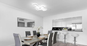 A modern dining area with a long table, chairs, and a vase of white flowers. - Coastal Comfort 2BR Retreat Balcony Space (Sunny Isles Beach)