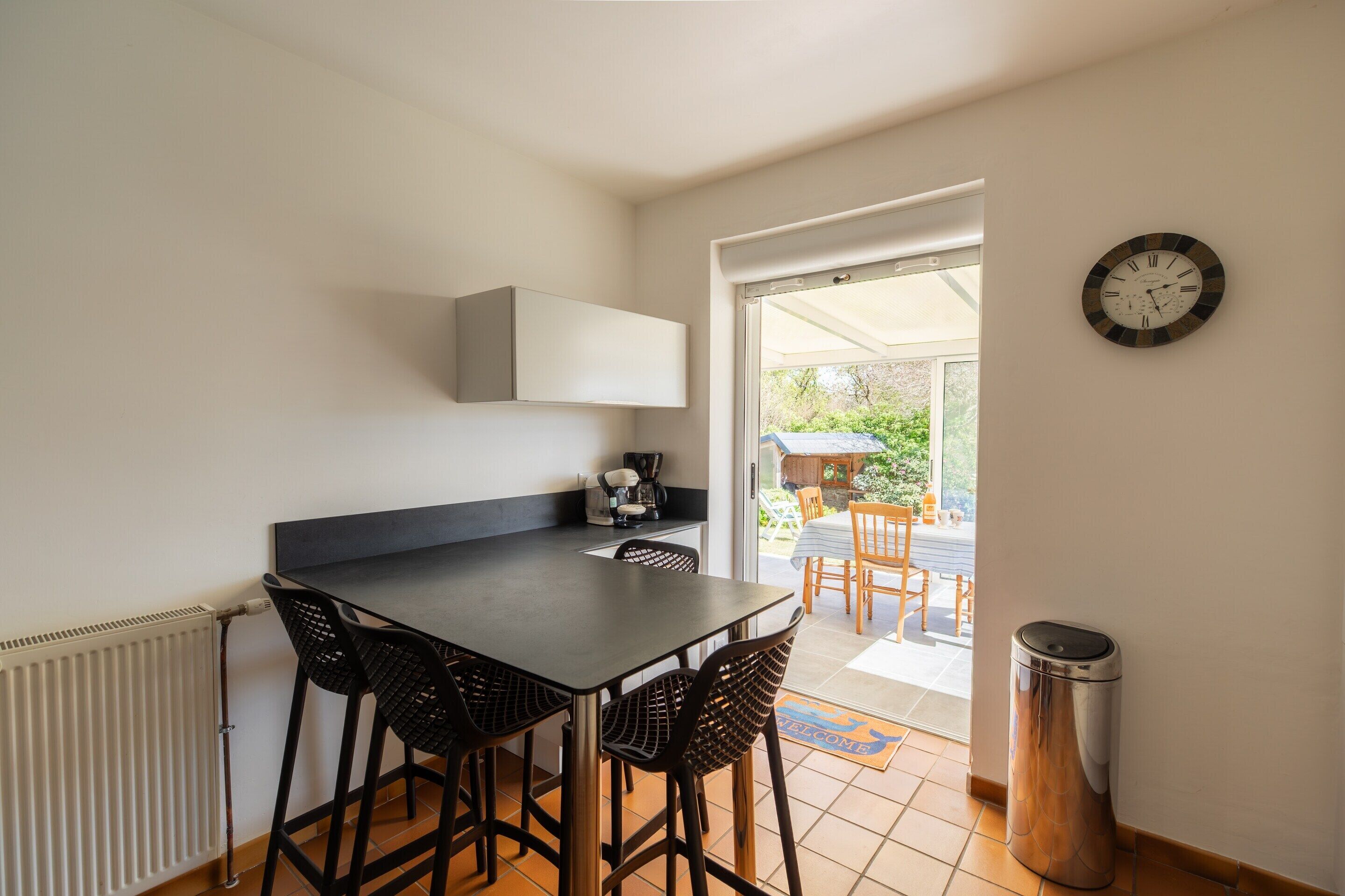Une petite cuisine avec une table et des chaises, un radiateur, une horloge et une porte donnant sur un espace extérieur.