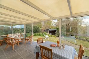 A covered patio with a table and chairs, a view of the garden, and a glass door leading outside. - Holiday Home for 9 in St. Renan (Saint-Renan)