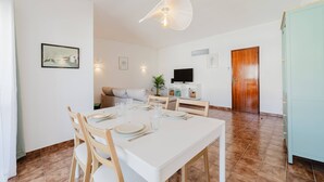 A dining area with a white table set for four, a sofa, a TV, and a wooden door. - Blue Stay - 1º D by HelloVacations (Albufeira)