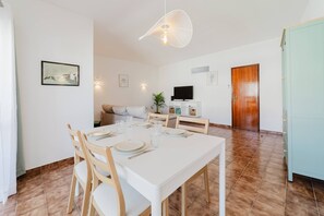 Ein Essbereich mit einem weißen Tisch, gedeckt für vier Personen, einer Couch, einem Fernseher und einer Holztür.
