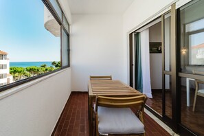 Ein Balkon mit Tisch und Stühlen, eine Schiebetür und Blick aufs Meer.