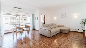A living room with a beige sectional sofa, a dining table with chairs, and a large window. - Blue Stay - 1º D by HelloVacations (Albufeira)