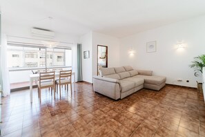 Ein Wohnzimmer mit einem beigefarbenen Ecksofa, einem Esstisch mit Stühlen und einem großen Fenster.