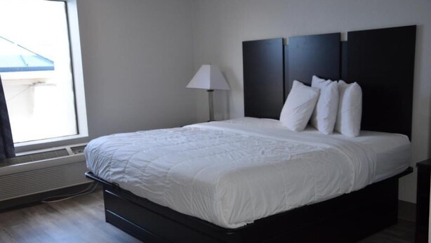 A modern bedroom with a large bed, a bedside lamp, and a window with blinds. - My Home and Suites Covington (Covington)