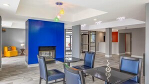 Un comedor moderno con mesa de vidrio y sillas azules, una chimenea y una pared de acento azul brillante.
