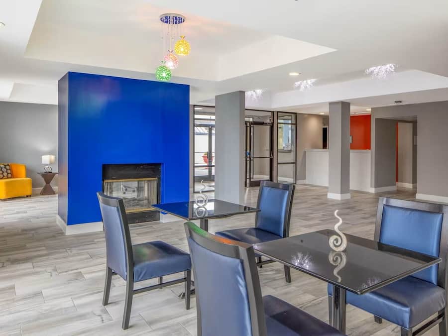 Un comedor moderno con mesa de vidrio y sillas azules, una chimenea y una pared de acento azul brillante.