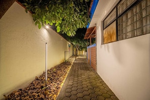 A narrow pathway with a tiled floor, bordered by walls and a tree overhead.