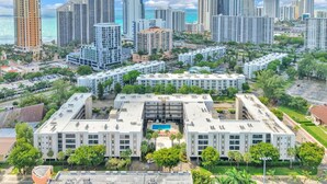 Un complejo de edificios altos con varias estructuras residenciales y comerciales, rodeado de vegetación y un cielo despejado.