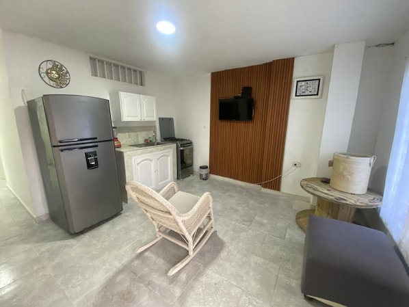 A compact kitchen with a refrigerator, a dining area with a chair, a small table, and a television mounted on a wall. - Apartment for 4 people (Cartagena de Indias)