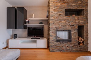 Ein modernes Wohnzimmer mit Fernseher, weißem Unterhaltungsschrank und einem Kamin aus Stein.