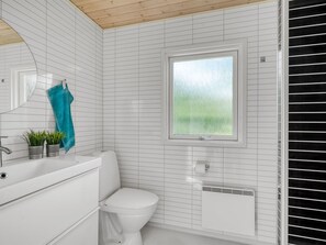 A bathroom with white tiled walls, a toilet, a window with a view, and a sink with a towel rack. - "Lucian" -  from the sea by Interhome (Hals)