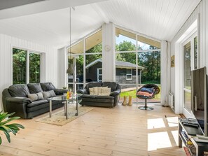 A spacious living room with a large window, a black leather sofa, a glass coffee table, and a small round table with a chair. - "Lucian" -  from the sea by Interhome (Hals)