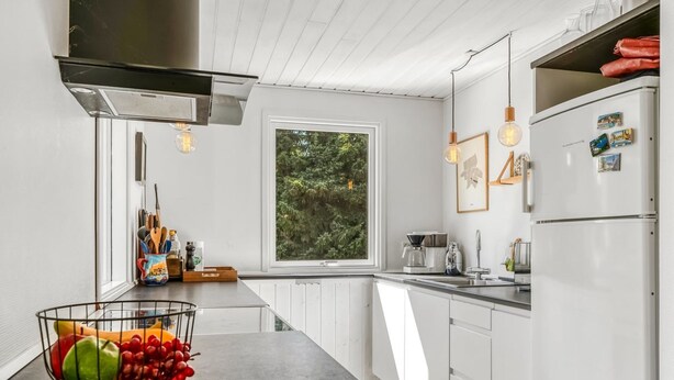 A modern kitchen with a central island, white cabinetry, a window with a view of greenery, and a stainless steel range hood. - "Lucian" -  from the sea by Interhome (Hals)