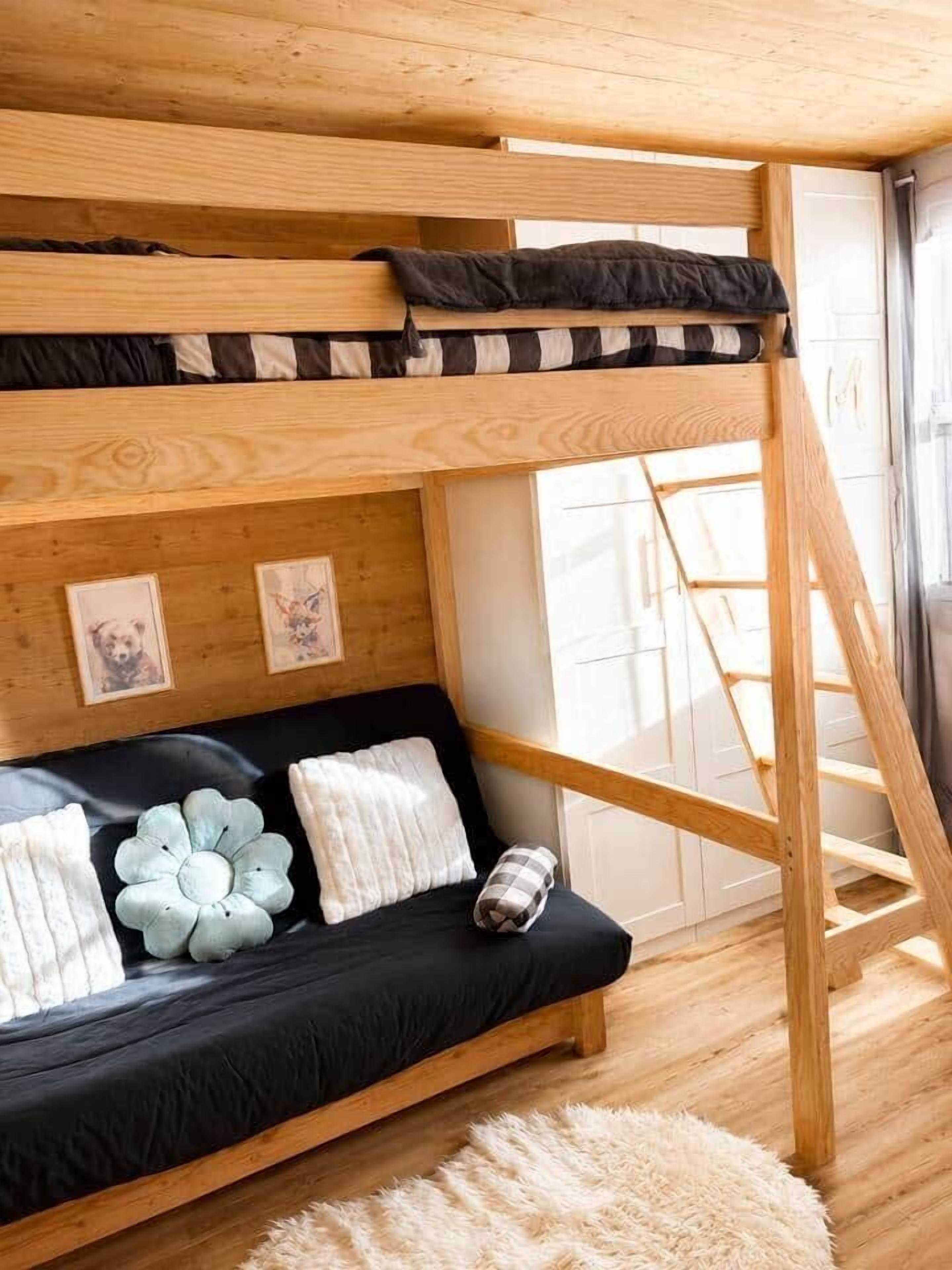 Una cama litera con un colchón y almohadas negras, una escalera de madera y una alfombra mullida sobre un suelo de madera.