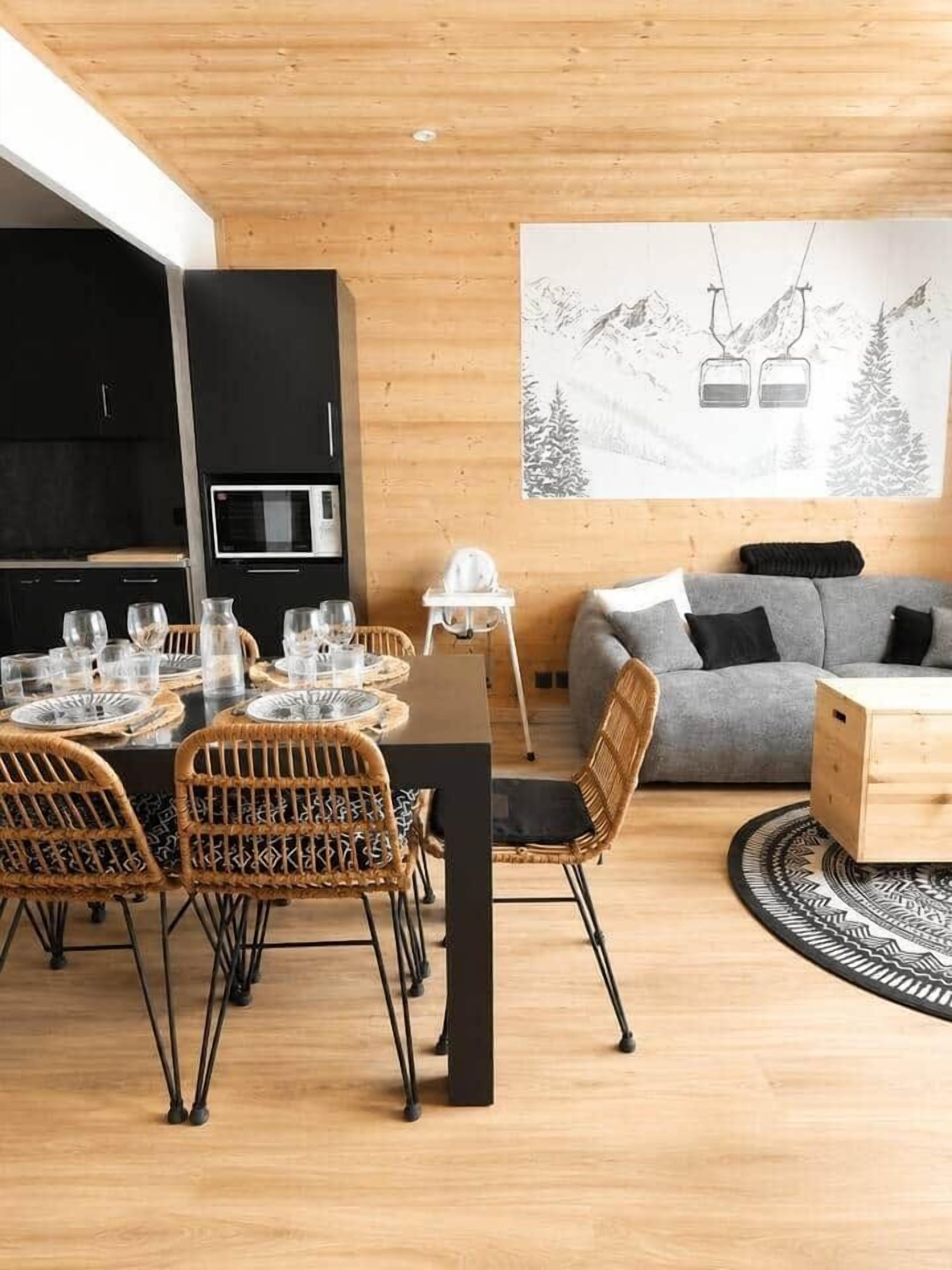 Ein modernes Interieur mit Essbereich, schwarzen Schränken, einem grauen Sofa und einem Gemälde von einer Berglandschaft.
